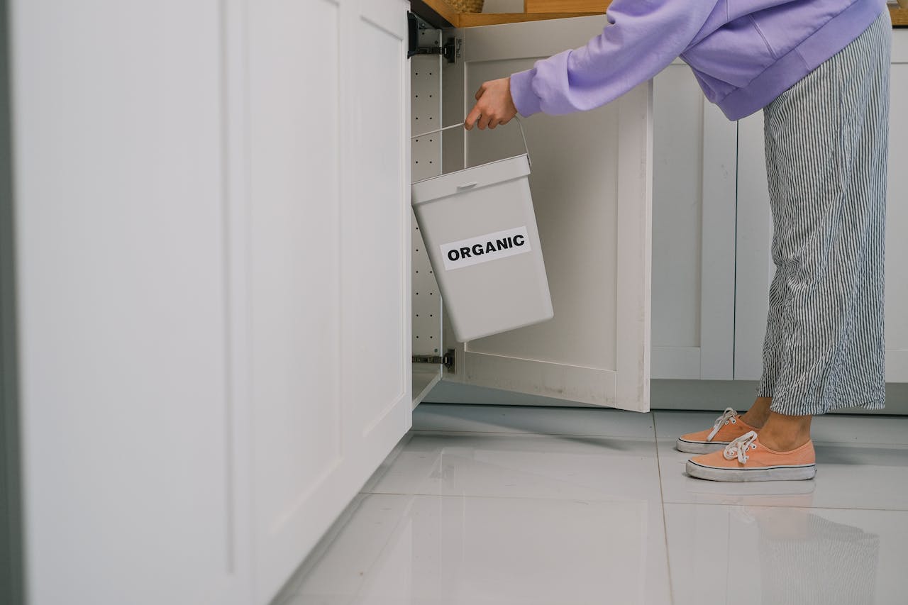 A person placing an organic waste bin inside a modern kitchen cabinet, promoting sustainable living.
